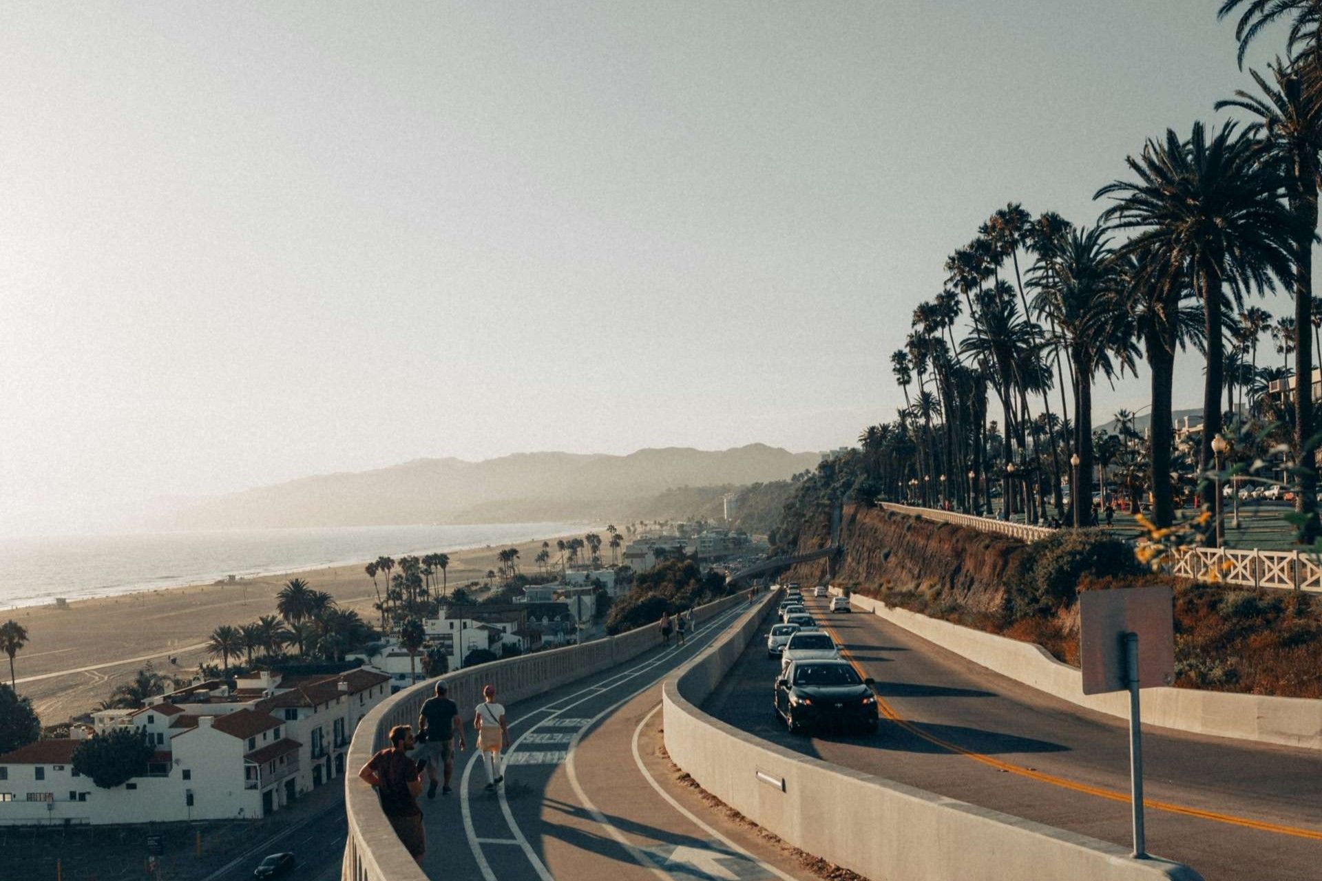 A street with cars and pedestrians is leading down hill towards Santa Monica Beach
